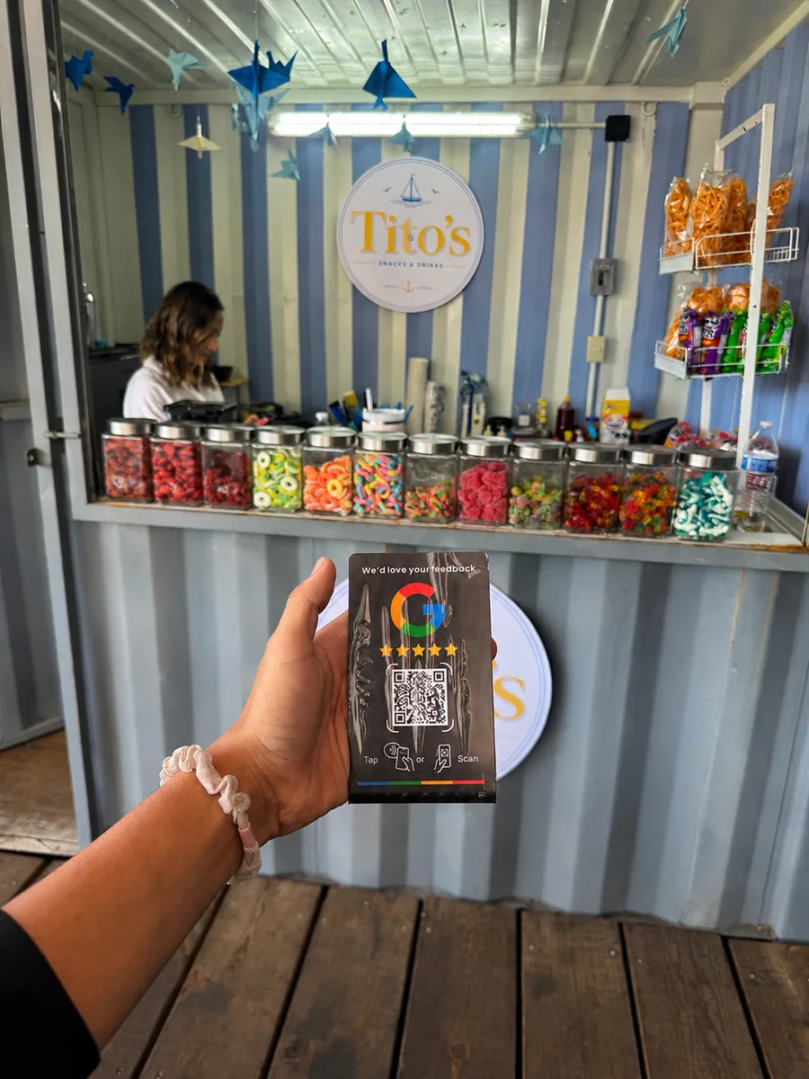 La placa frente al mostrador de Tito’s Snacks & Drinks: un local de dulces con la hilera de botes de cristal y el rótulo del negocio al fondo.